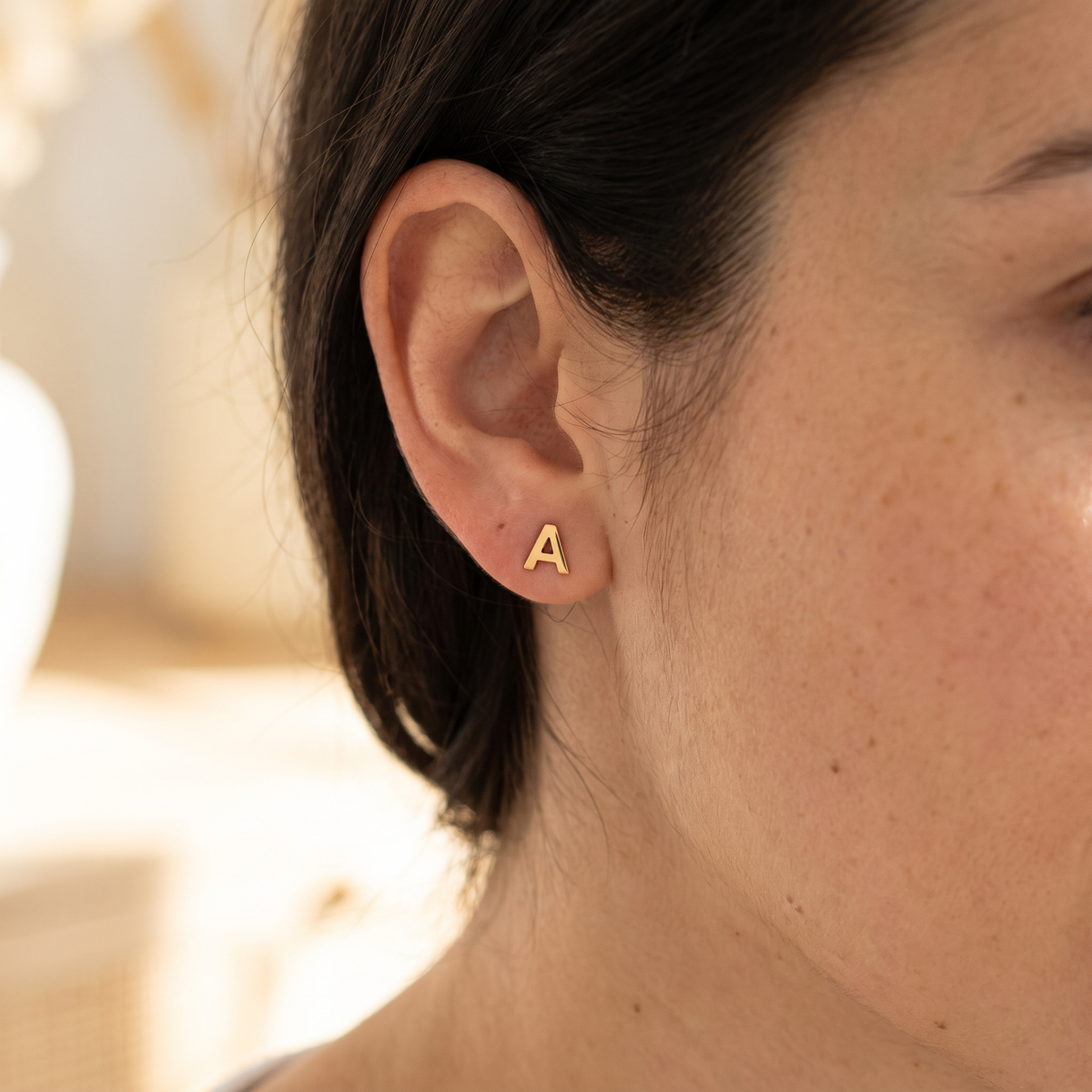 Boucle d'oreille à l'initiale portée, cheveux ramenés derrière l'oreille