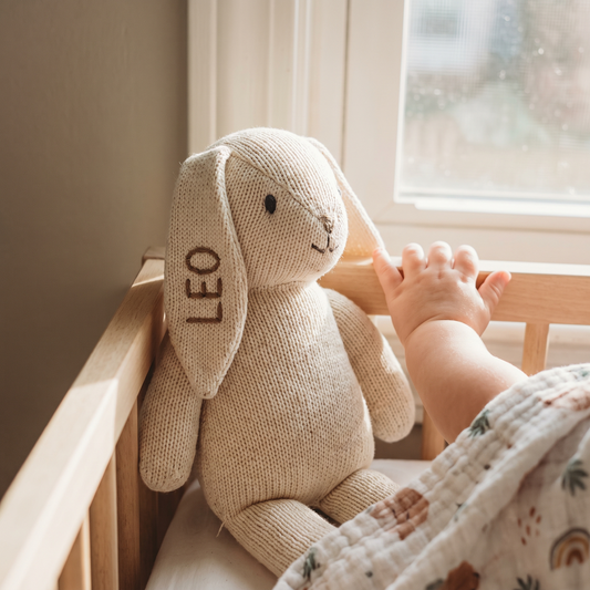 Lapin en peluche de tricot brodé au prénom, dans un lit de bébé