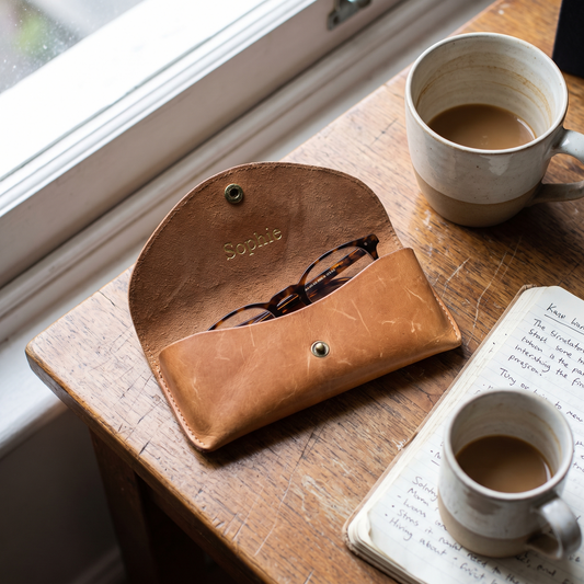 Étui à lunettes en cuir fauve gravé d'un prénom, ouvert sur un bureau avec des lunettes de lecture