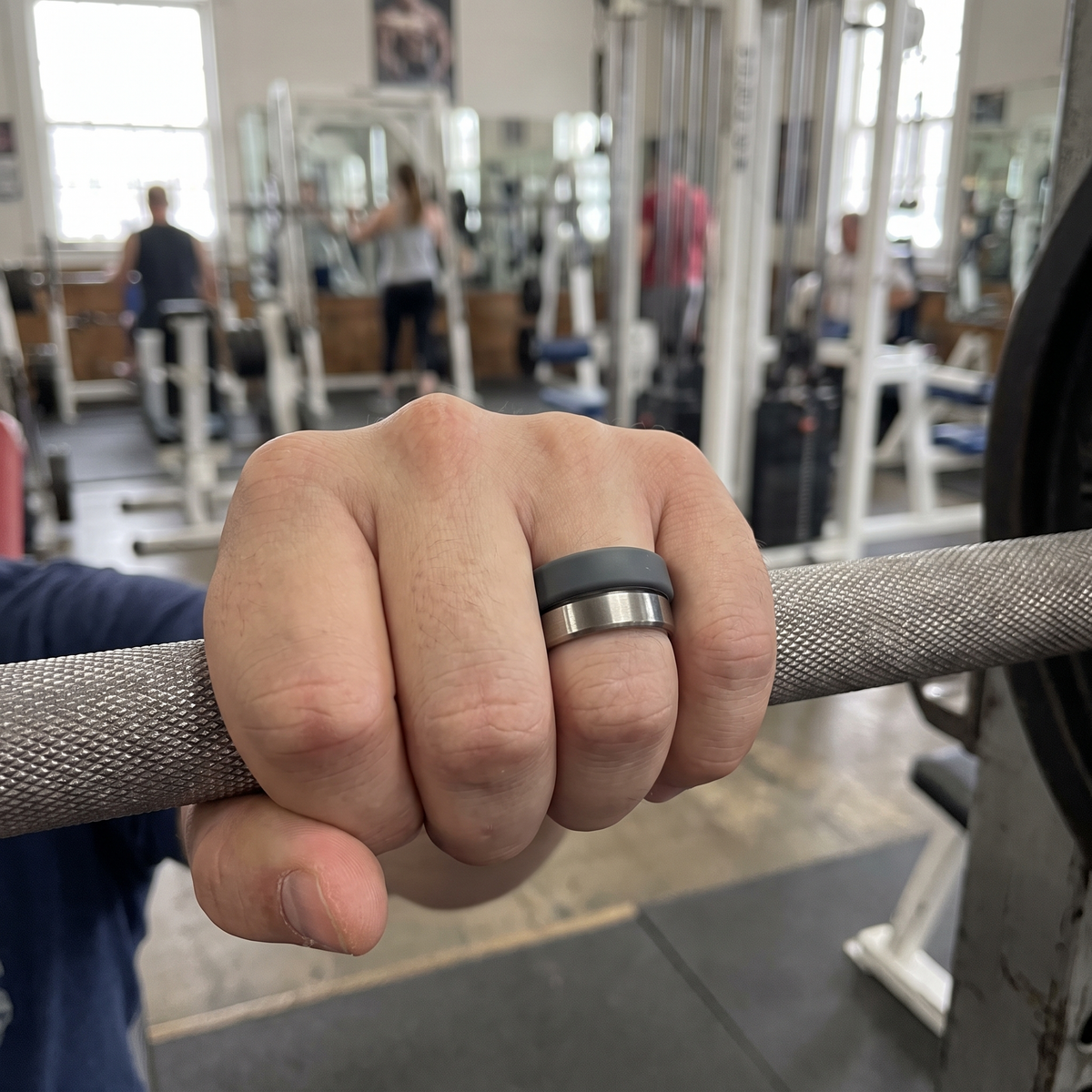 Main sur une barre de gym portant une bague connectée protégée par un couvre-anneau